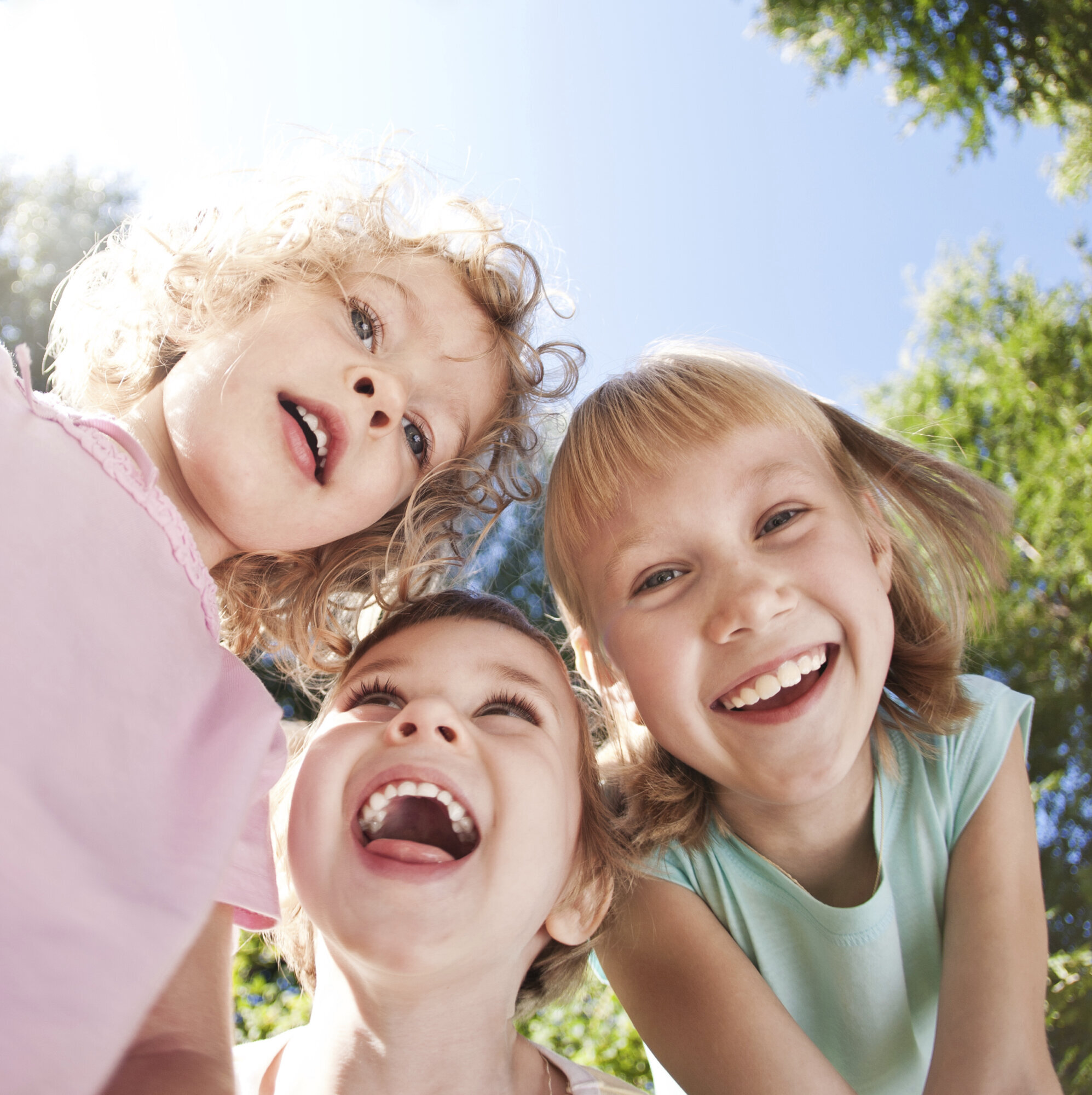 Bild von drei Kindern, die von oben in eine Kamera lachen.